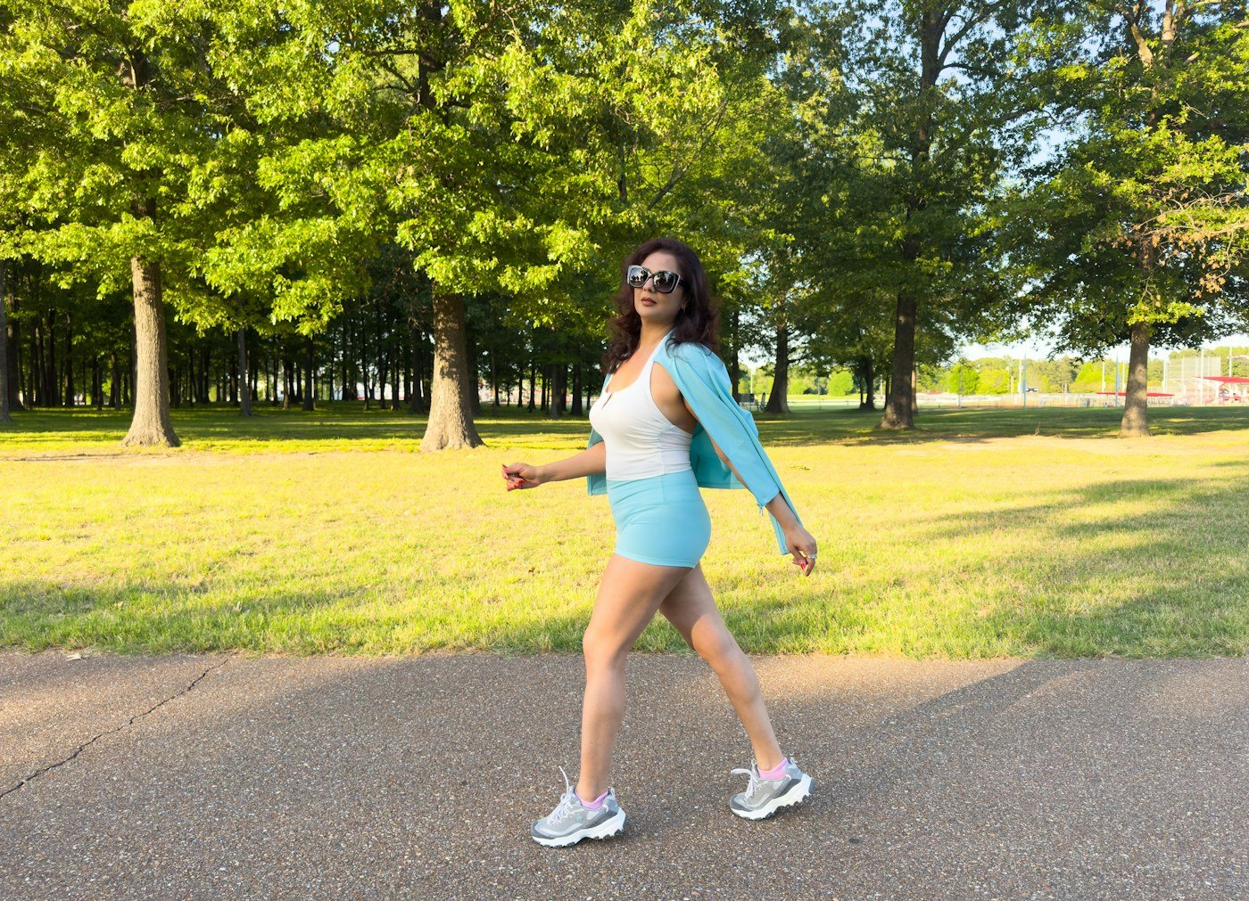 Woman walking on a paved path through a green park